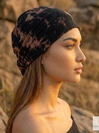 A woman in profile wears a black and brown tie-dye headwrap, standing outdoors among rocks at sunset. The lighting highlights her facial features and long hair. A small KVK Boho Fair logo is visible in the bottom right corner.