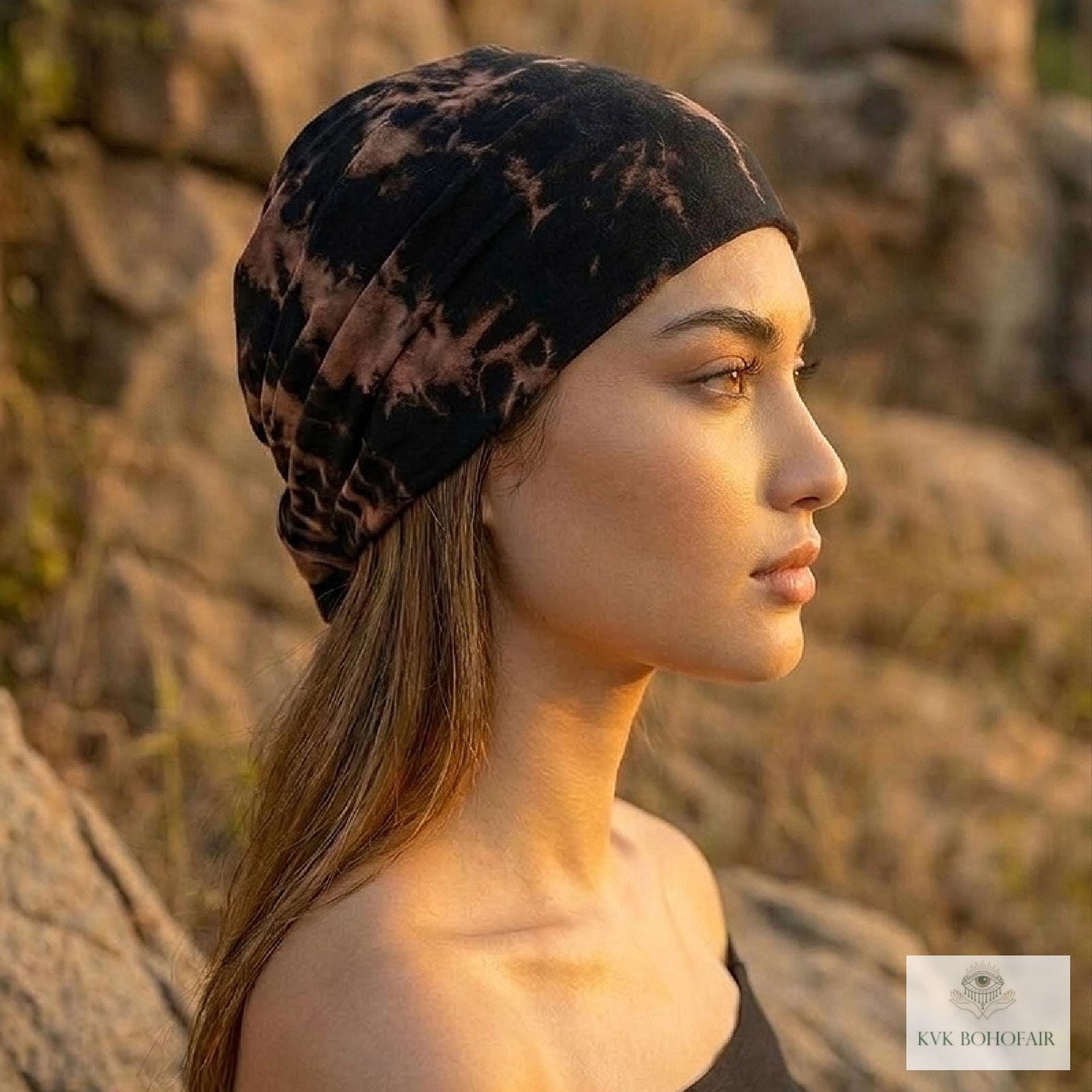 A woman in profile wears a black and brown tie-dye headwrap, standing outdoors among rocks at sunset. The lighting highlights her facial features and long hair. A small KVK Boho Fair logo is visible in the bottom right corner.